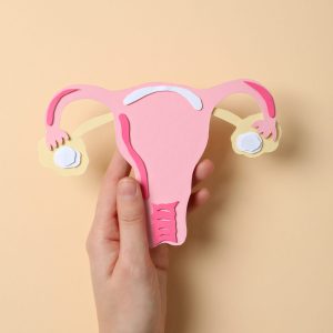 Paper uterus in female hand on beige background, top view